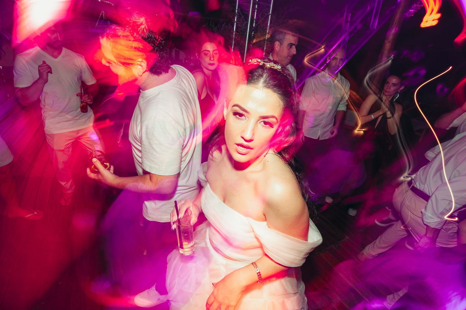 Nightclub scene with vibrant pink and purple lighting showing people dancing on a crowded dance floor.