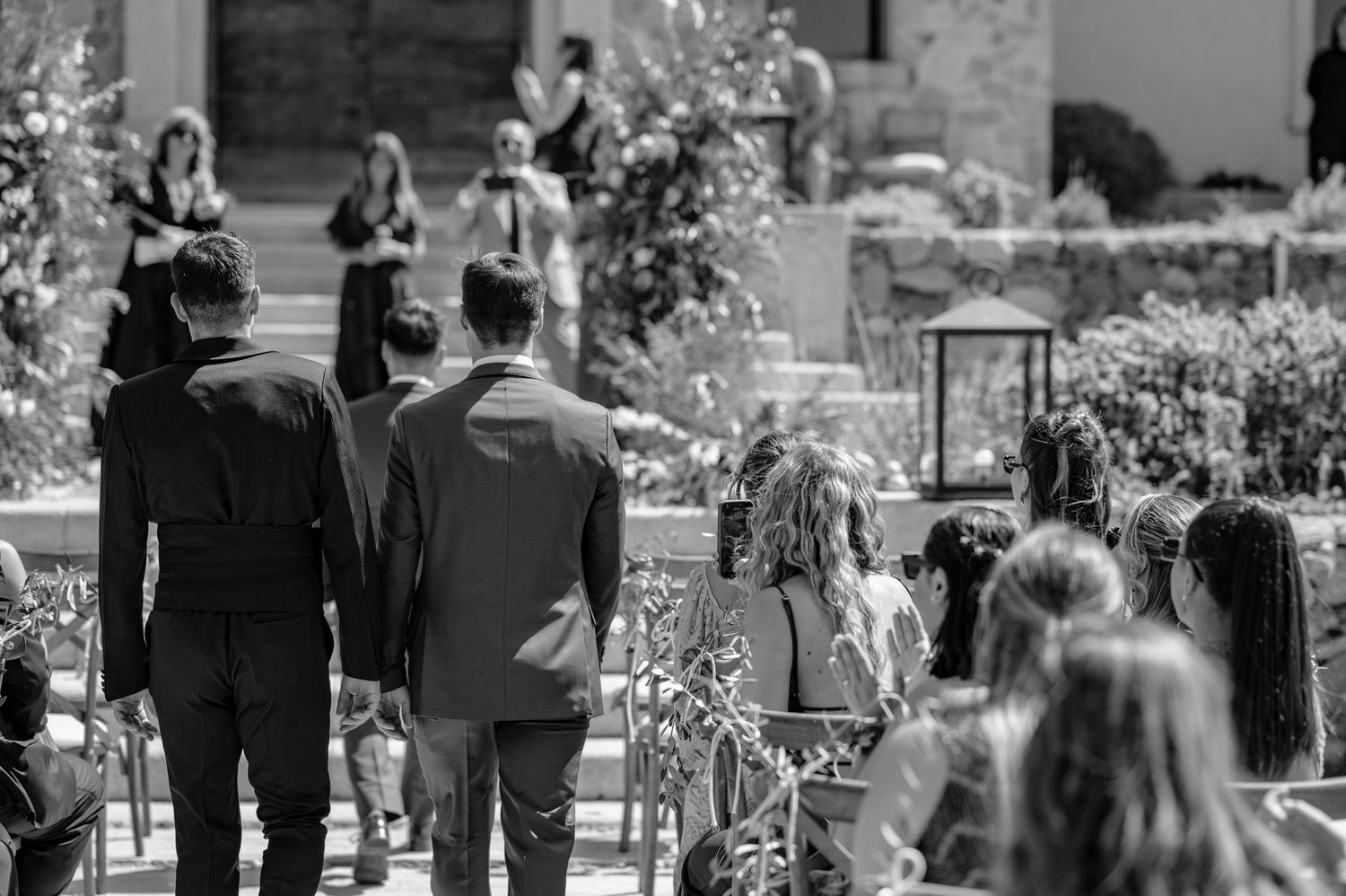 Black and white photo showing people walking and gathering outdoors in what appears to be a garden or park setting.