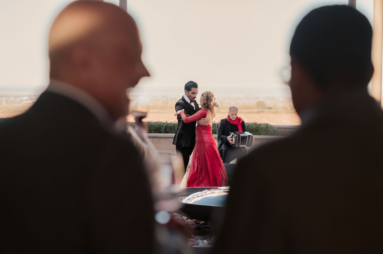 Couple sharing a romantic dance in elegant attire, woman in red gown, at an upscale indoor venue with guests watching.