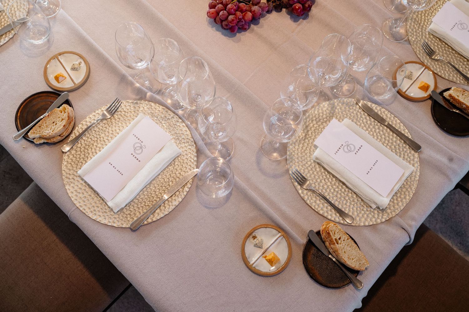 Elegant wedding table setting with gold charger plates, crystal glasses, white menus, and fresh grapes centerpiece.