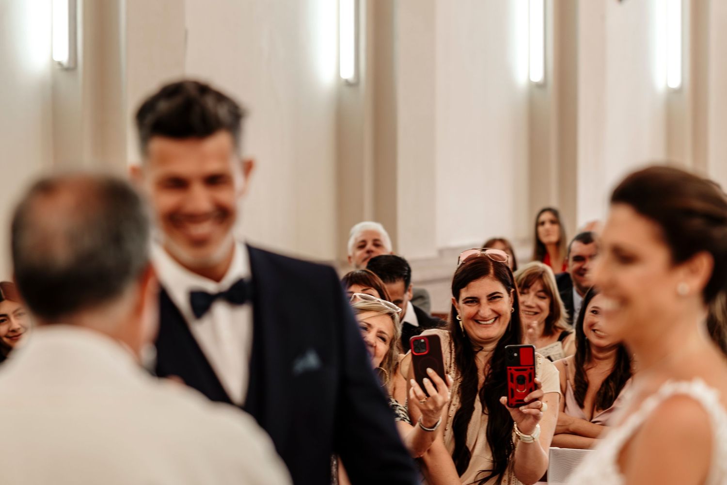 Wedding guests laugh and celebrate during a joyous reception in an elegant white ballroom.