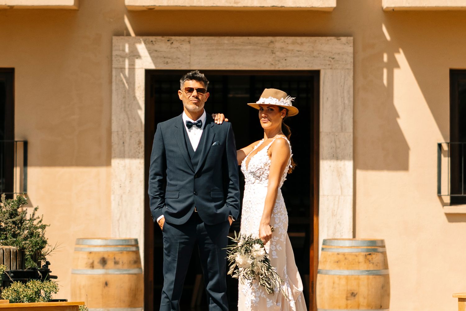 A couple in elegant wedding attire shares a romantic moment under a Mediterranean-style archway with warm lighting.