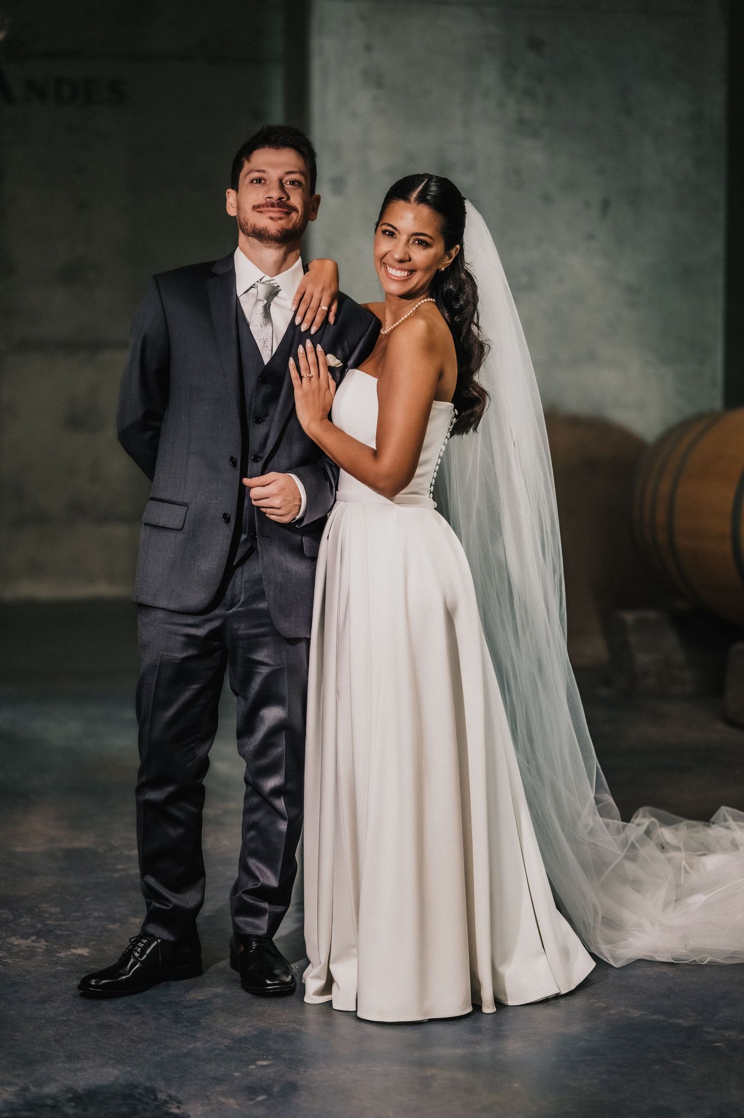 Elegant bride in white gown with veil and groom in gray suit posing together at a winery wedding venue.
