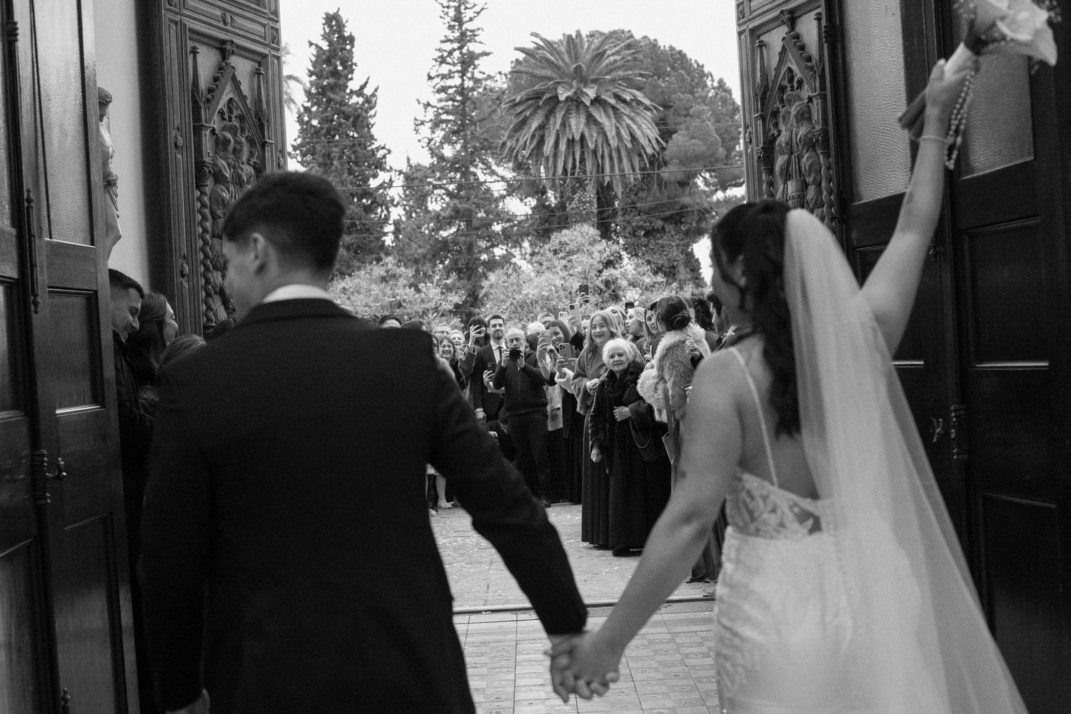 Black and white photo of bride and groom holding hands entering church doors at their wedding ceremony.
