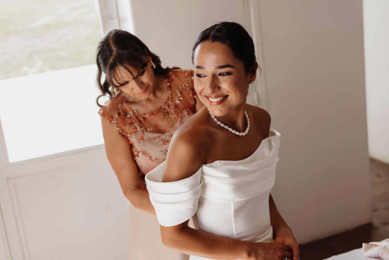 A couple in white clothing embraces and laughs together in a bright indoor setting.