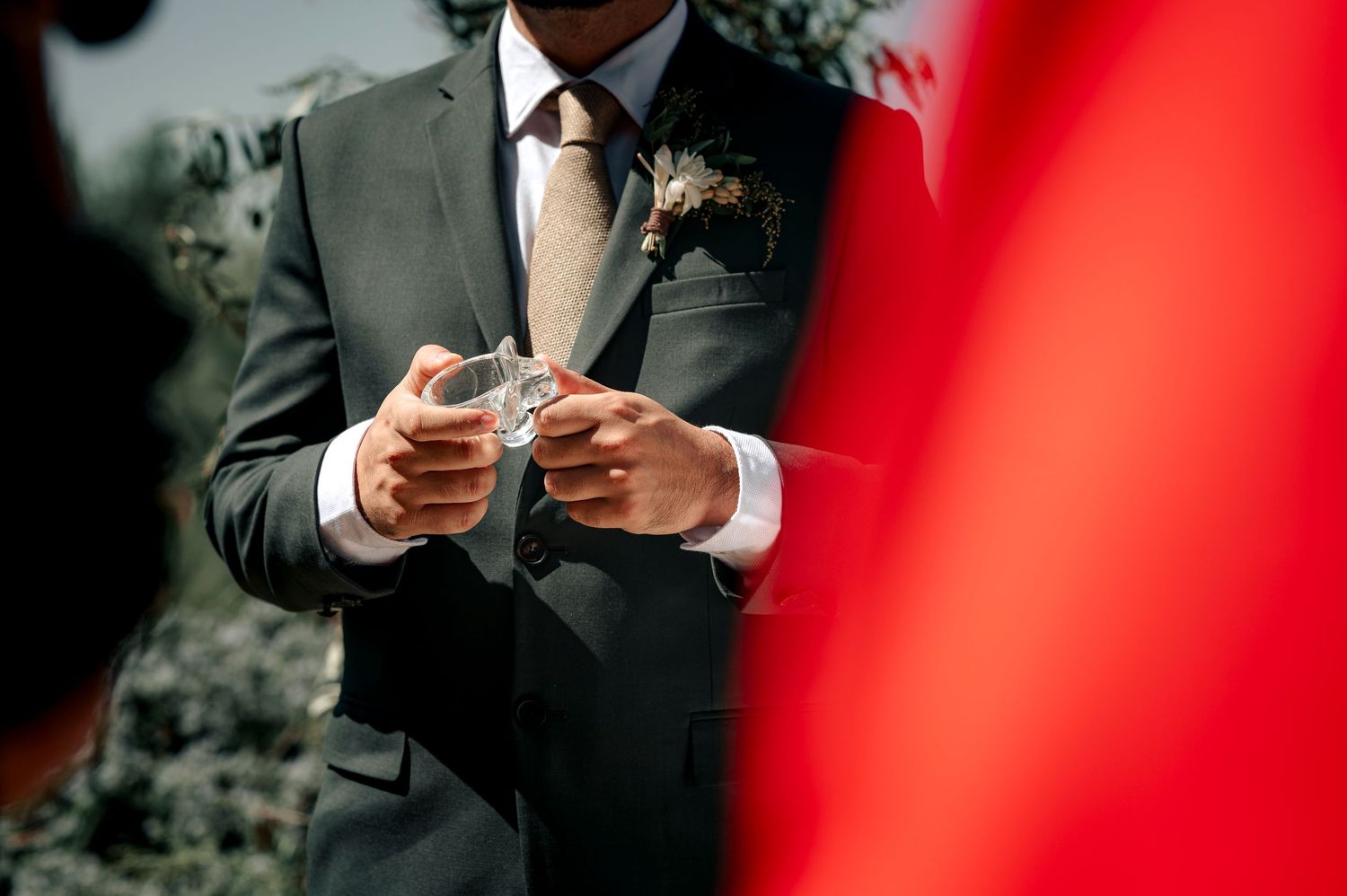 A person in a gray suit holding a phone at an outdoor event, with a red blur in the foreground.