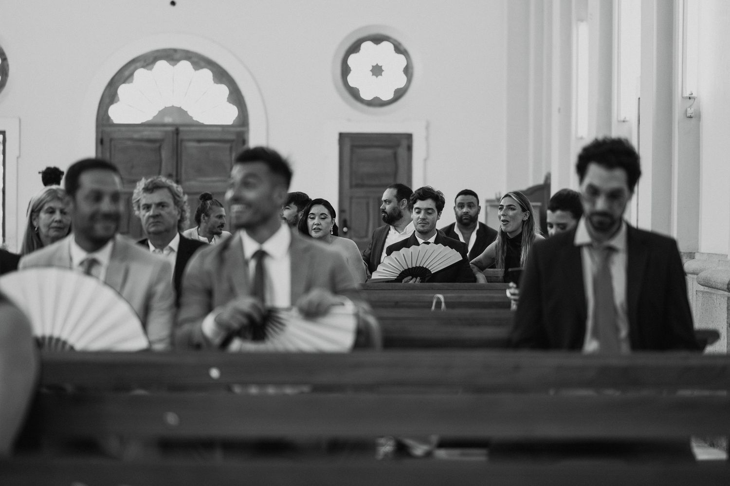 Black and white photograph showing people seated in wooden pews inside a church or courtroom setting.