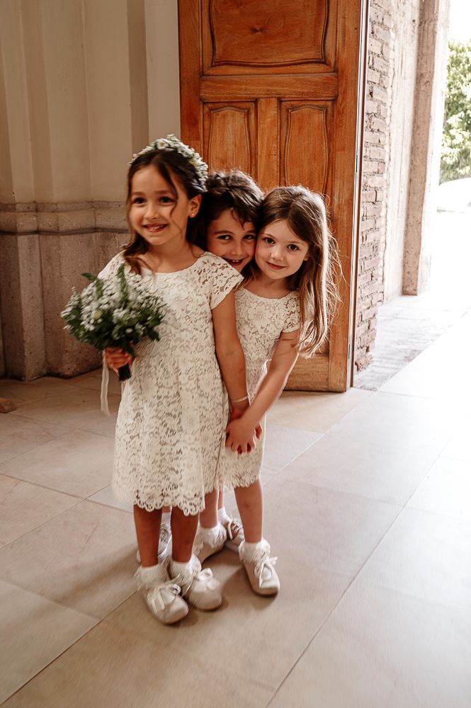 Three young attendants in matching white lace dresses and floral crowns pose together at a wedding ceremony. wedding in mendoza