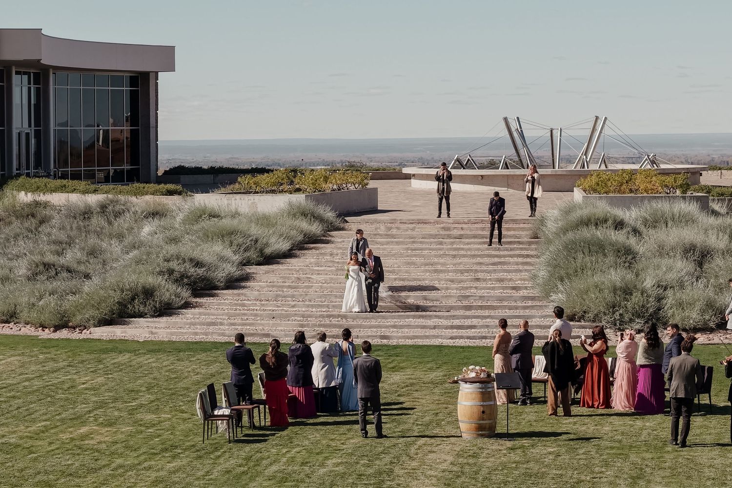 Outdoor wedding ceremony on a terrace overlooking the ocean, with guests gathered around the couple on a sunny day. fotógrafos de boda