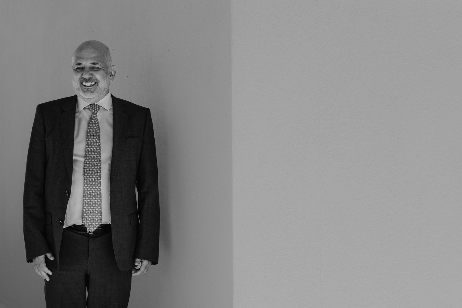 Professional businessman in dark suit and tie smiling confidently against a neutral gray background.