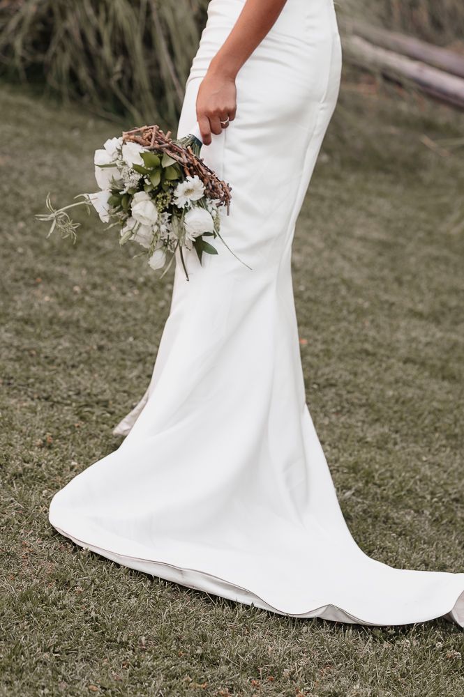 Close-up view of white wedding dress train and bouquet details on grass showing delicate floral arrangements and fabric texture.  wedding in