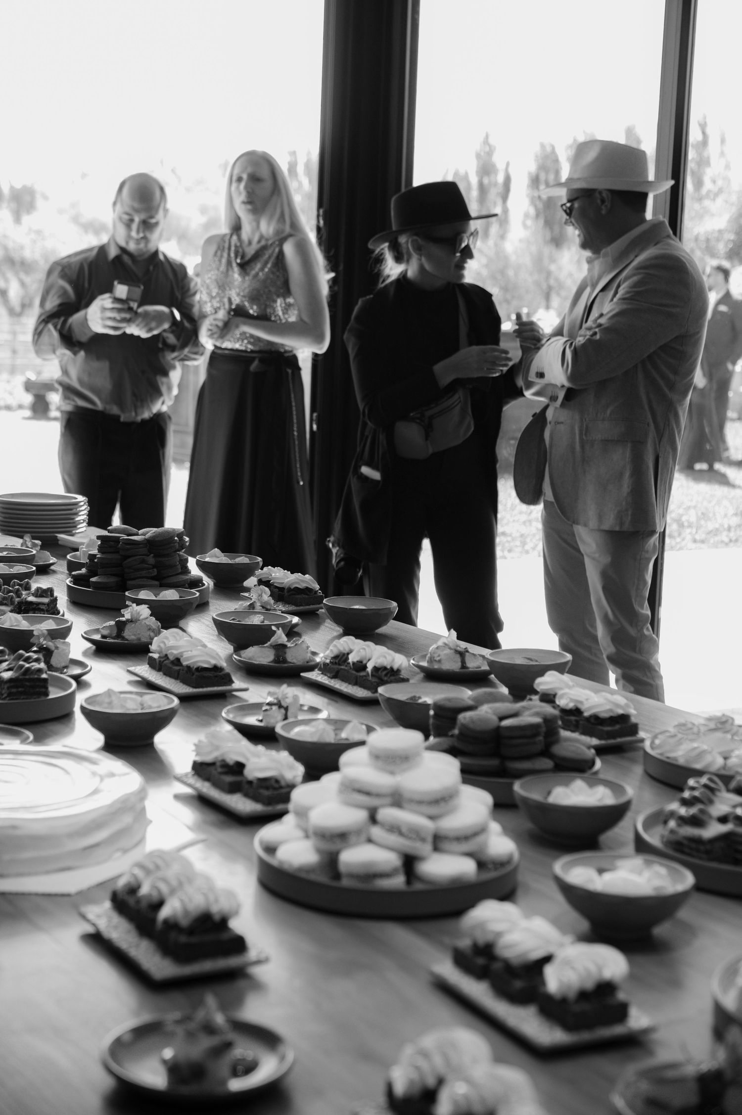 A black and white photo series showing plates of food on a buffet table with people gathering in the background.