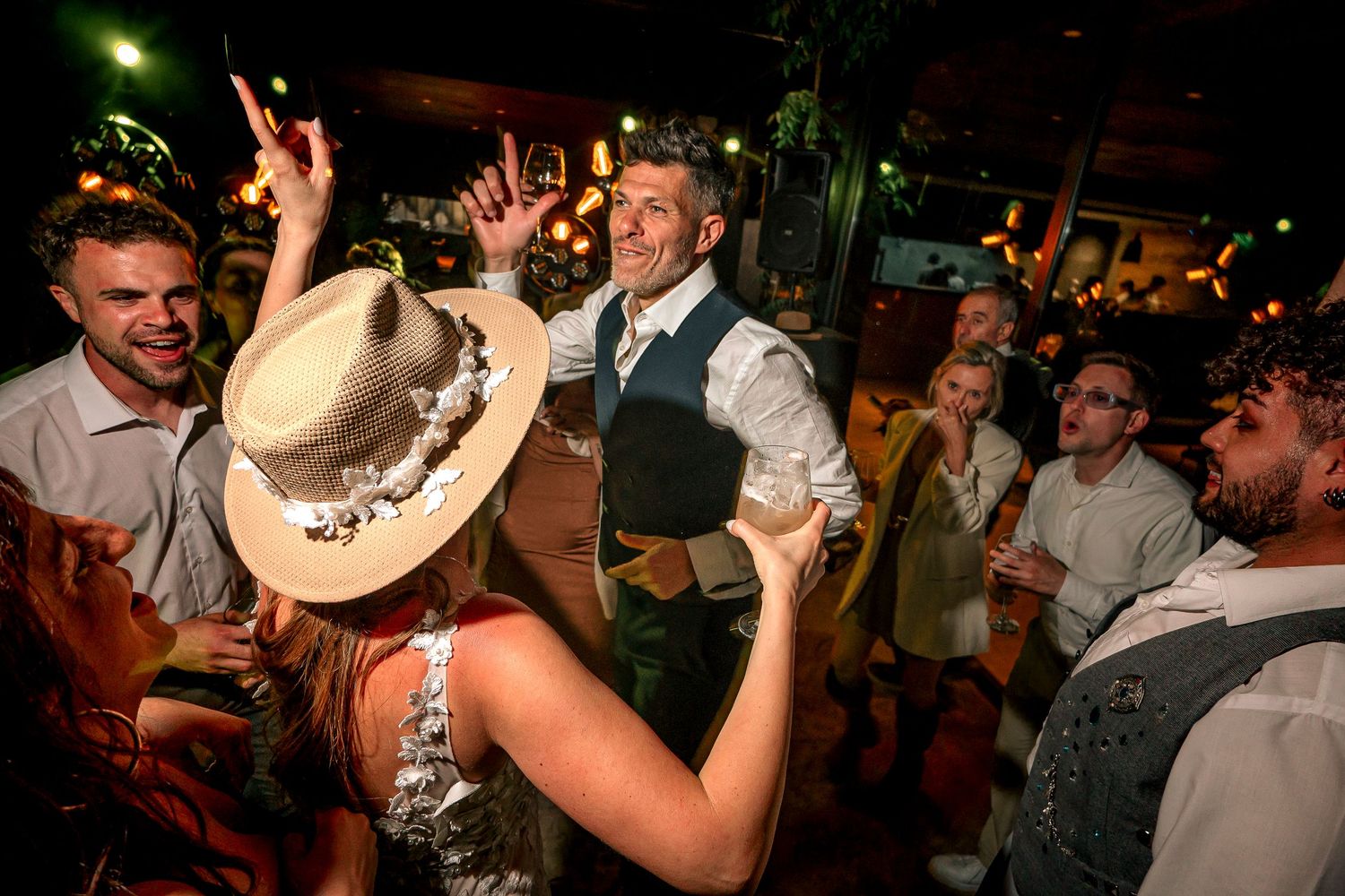 Energetic crowd celebrates at a nighttime wedding reception with cowboy hat and dancing.