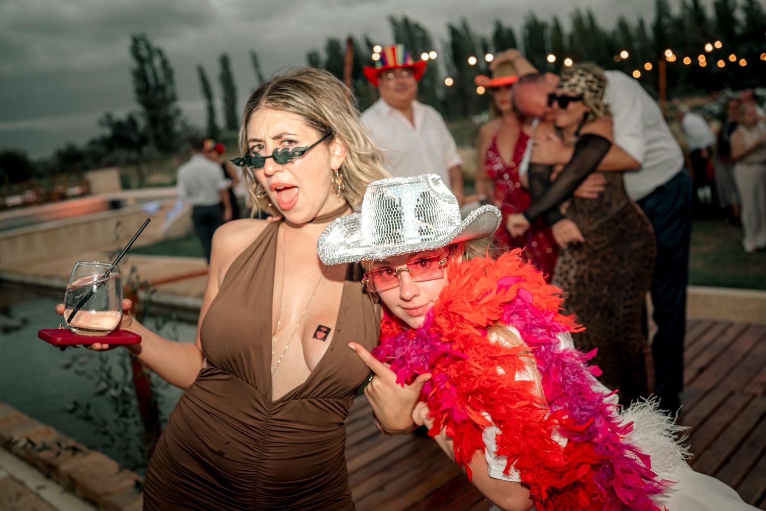 People dancing and celebrating at an outdoor party with red feather boas and festive decorations at dusk.