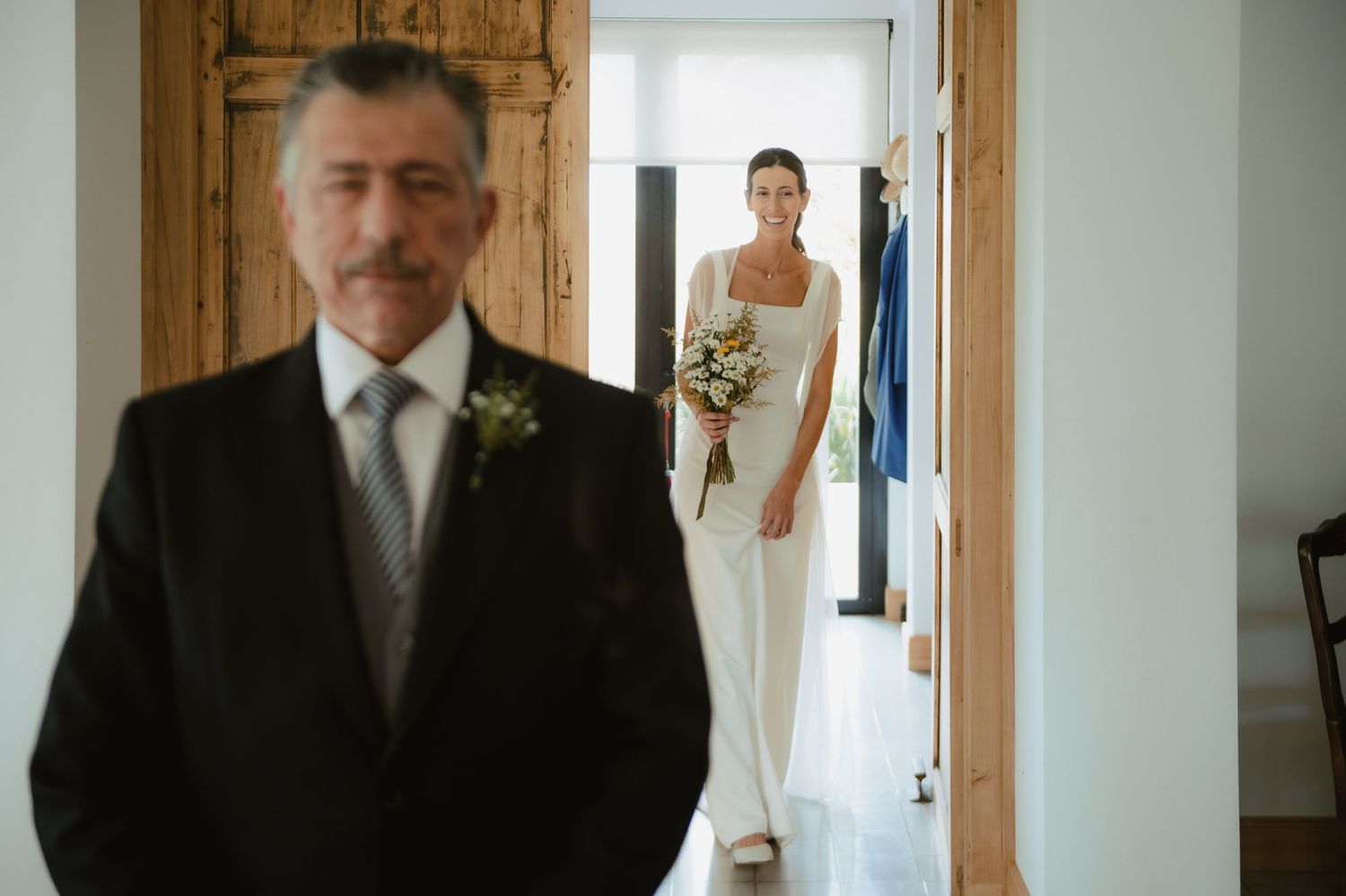 A group of well-dressed people stand near wooden doors in a white hallway before a wedding ceremony.