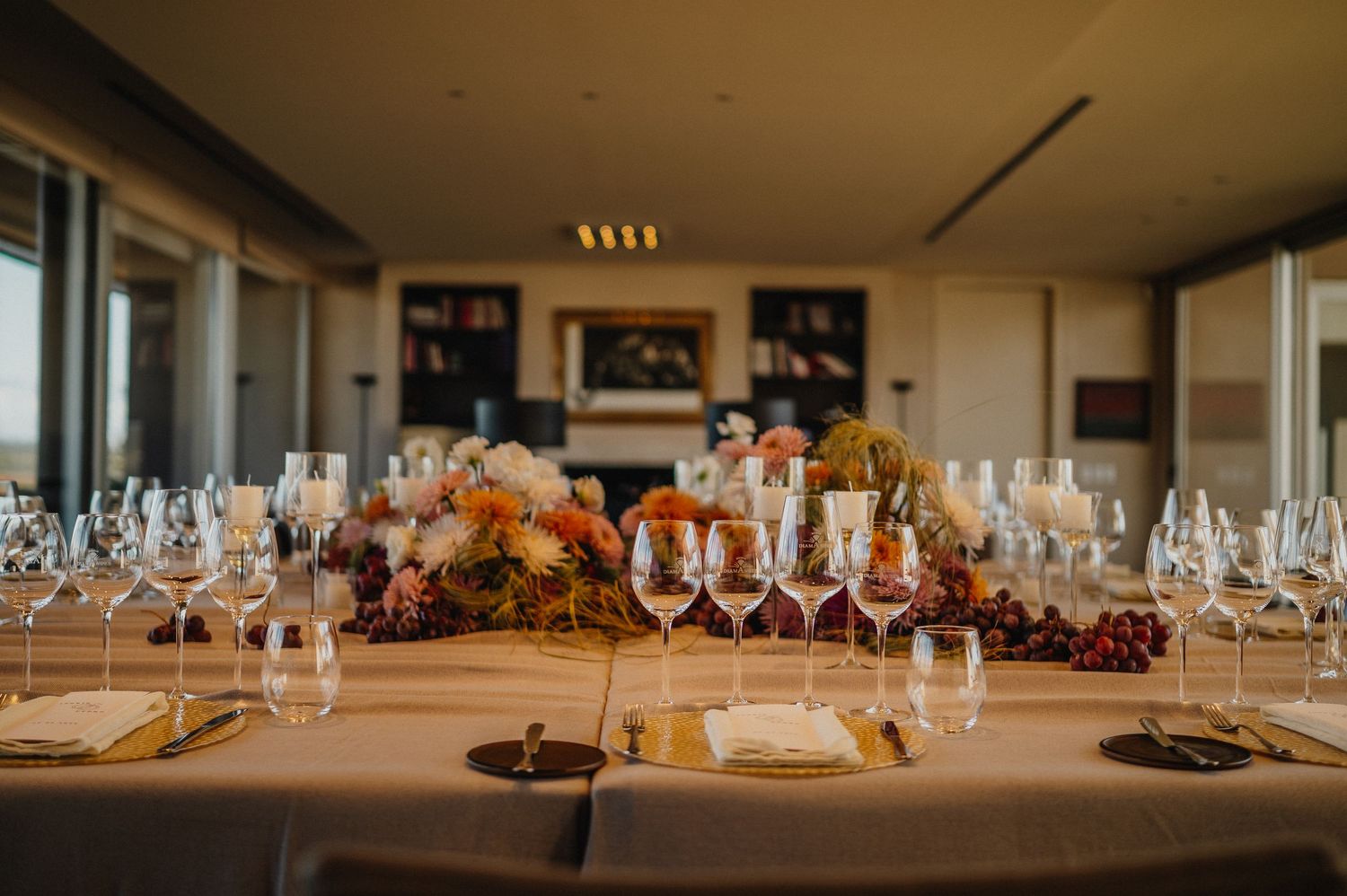 Elegant dining table set with crystal wine glasses and autumn floral centerpiece in a warmly lit restaurant.