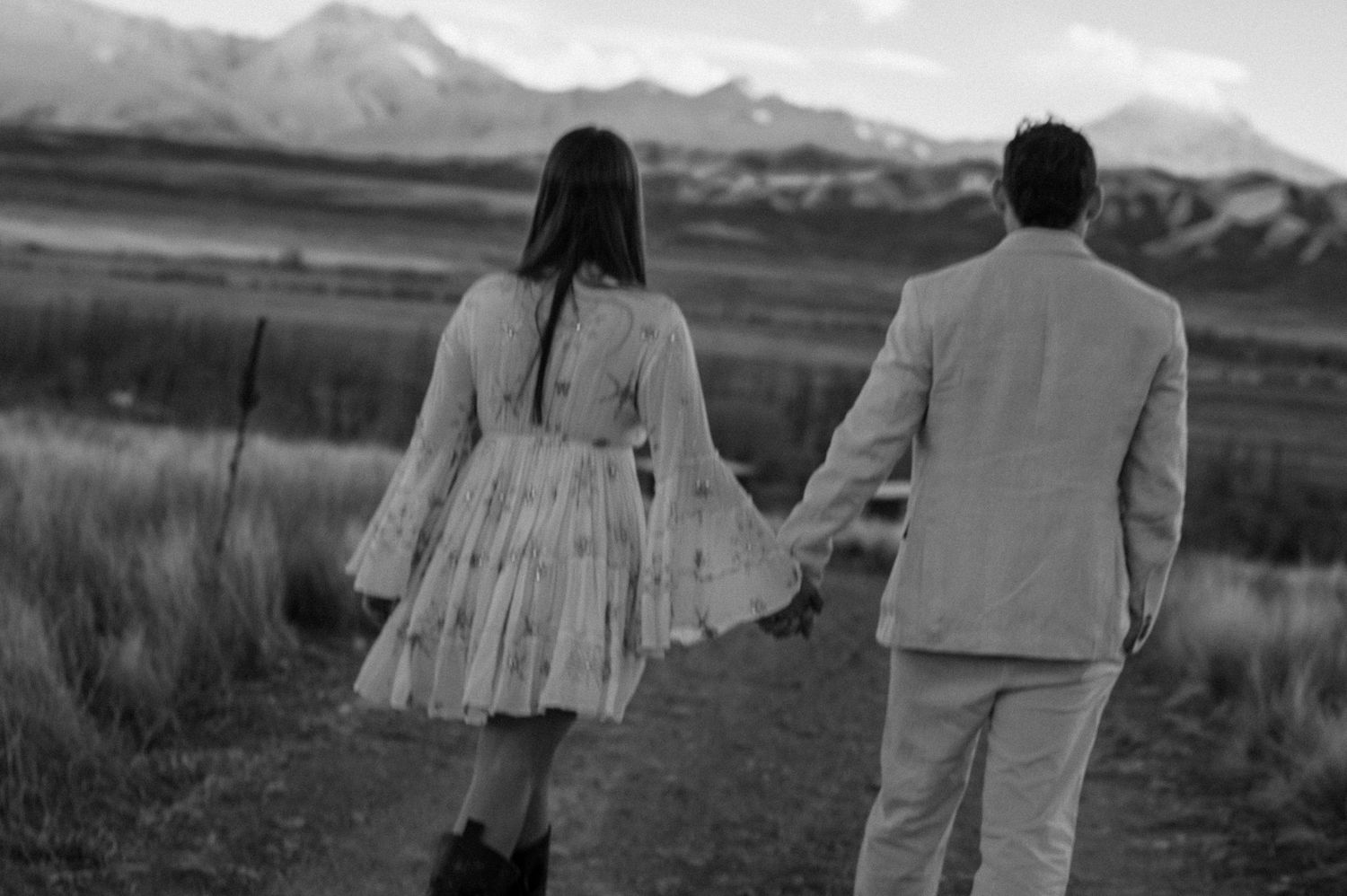 Fotografía en blanco y negro de una pareja tomada de la mano caminando hacia un paisaje montañoso en un campo abierto. pre boda en mendoza