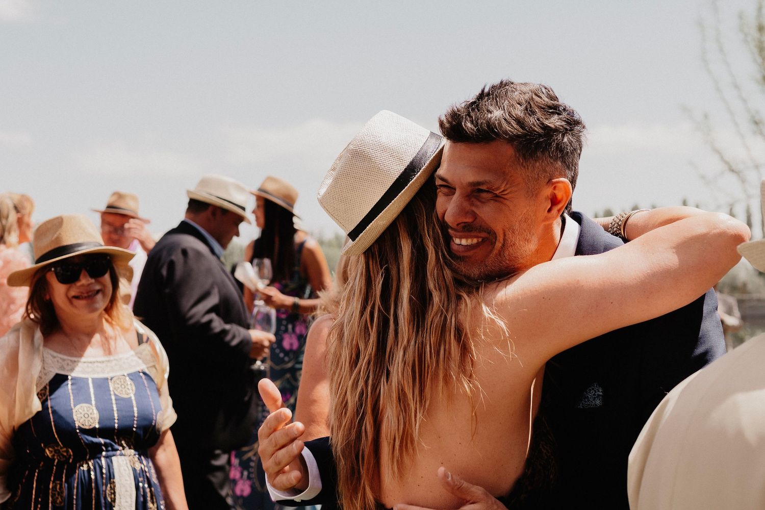A group of people dancing and celebrating at an outdoor wedding reception in natural lighting.