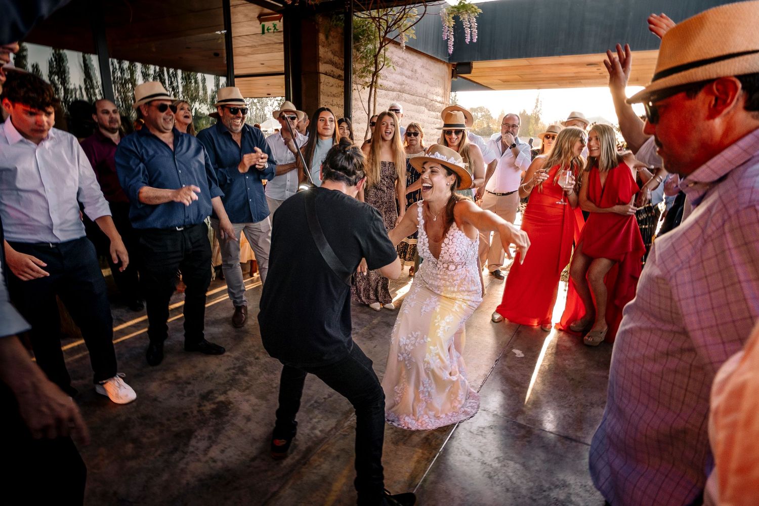 Wedding guests dancing and celebrating on a rustic wooden dance floor at an outdoor venue during sunset.