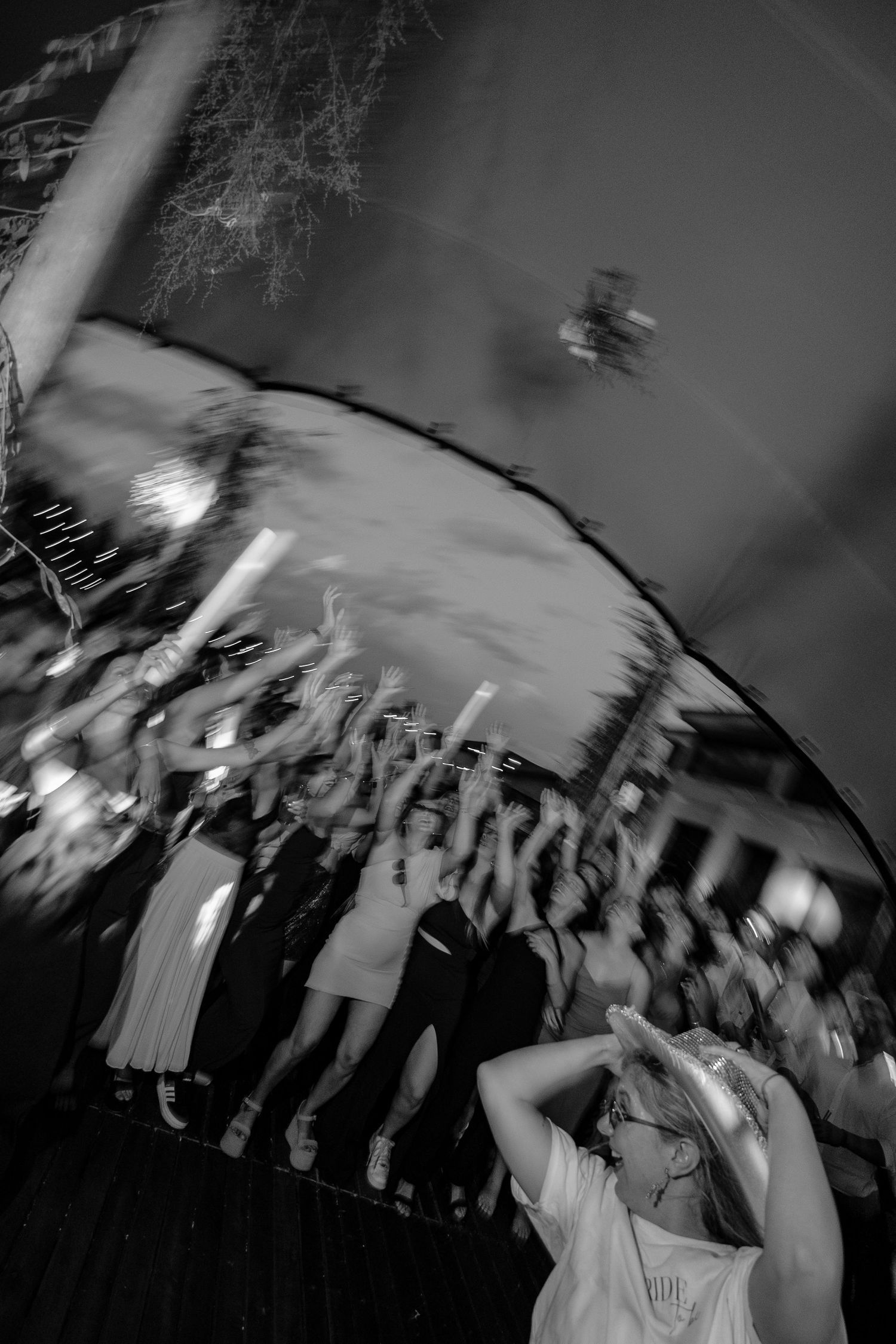 A blurred black and white photo of people dancing at a party or celebration with motion captured movement.