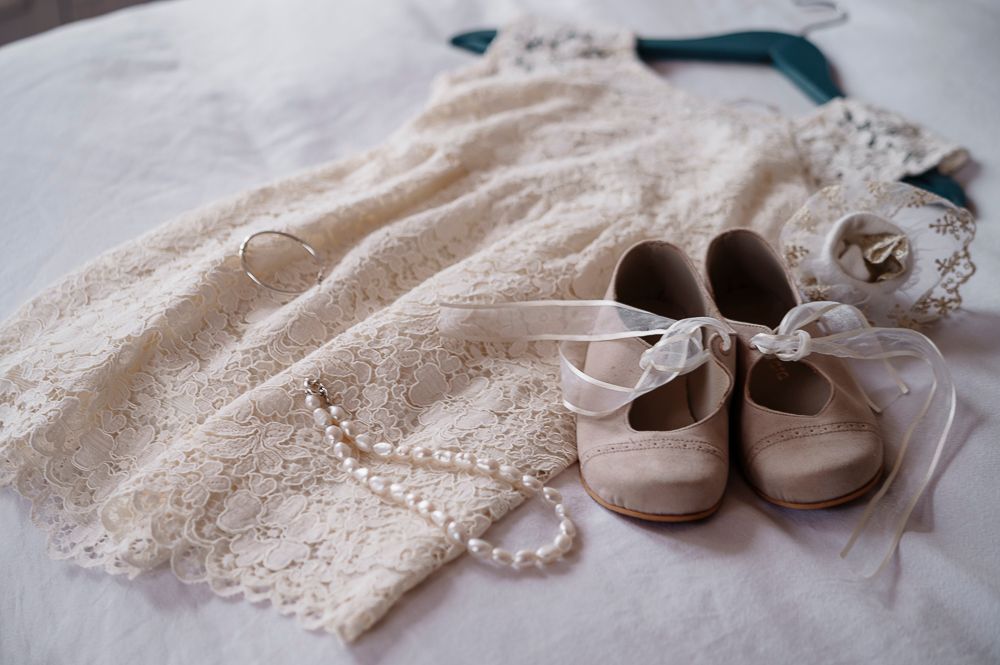 Vintage lace fabric and brown leather baby shoes arranged in a delicate flat lay composition.