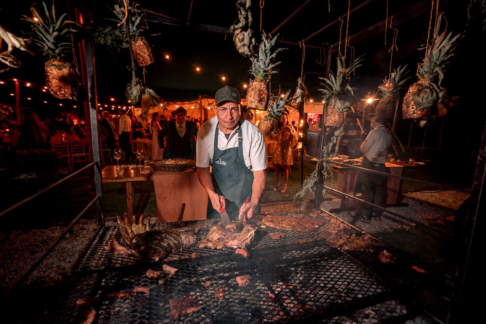 Chefs prepare food at an outdoor nighttime barbecue event with glowing embers and flames illuminating the scene. wedding in mendoza