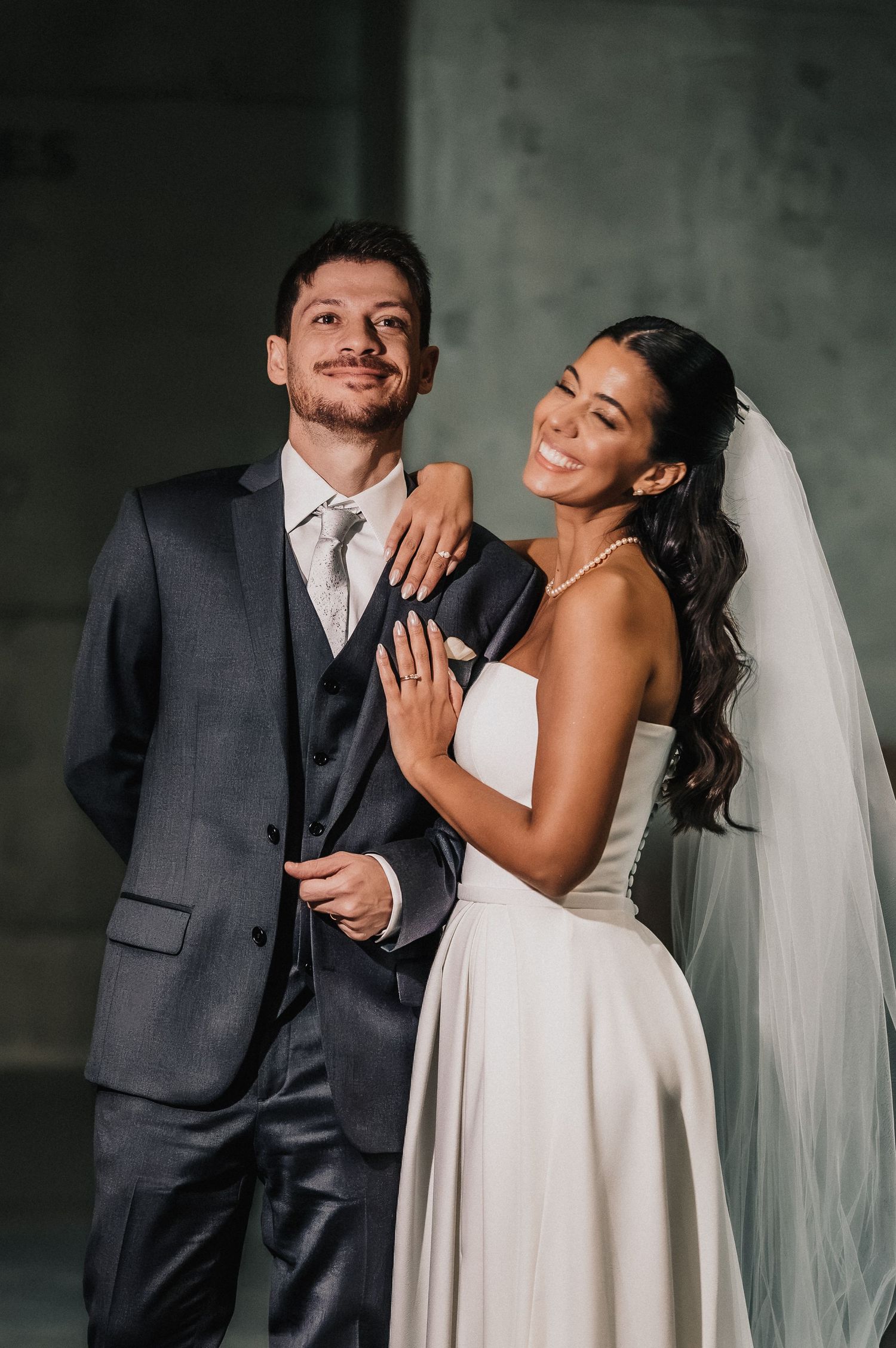 A smiling bride in a white gown and veil poses with a groom in a gray suit during their wedding portrait. fotógrafos de boda Mendoza