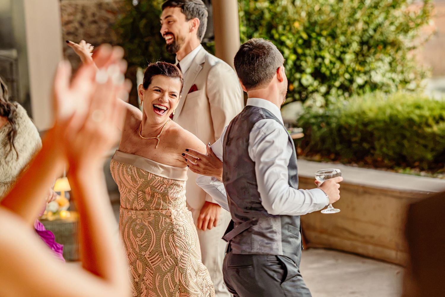Bride in gold gown laughs joyfully with groom in tan suit at outdoor wedding reception celebration.