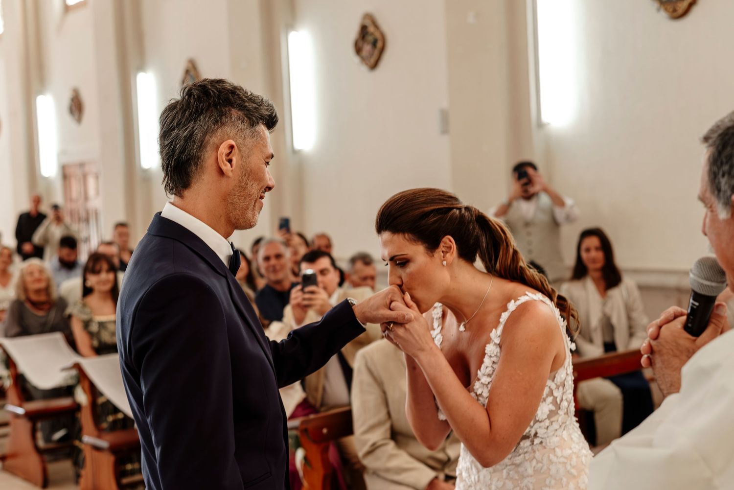 A couple shares their first dance at a wedding reception while guests watch and take photos with their phones.