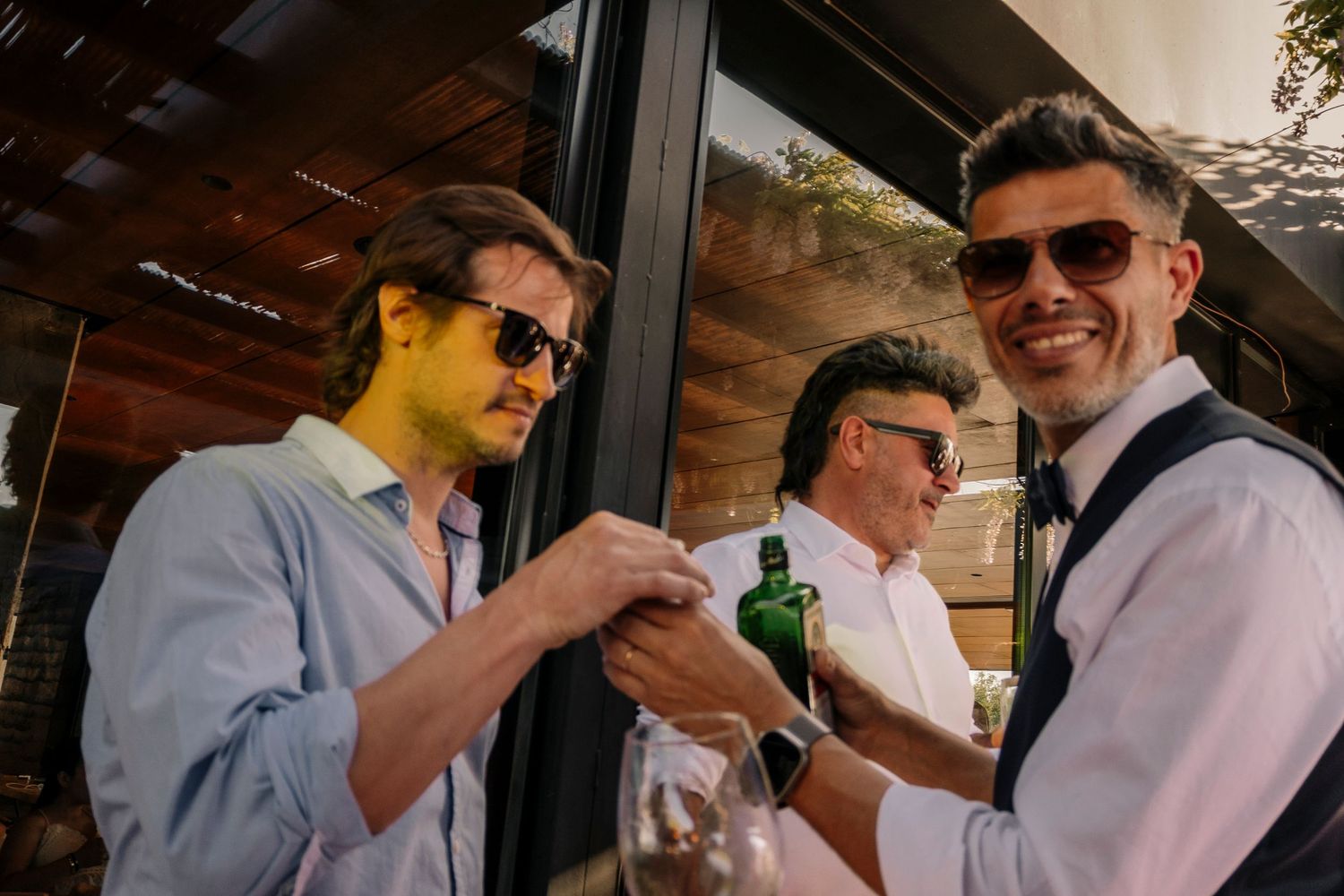 A group of people in light blue shirts and sunglasses stand together holding drinks at an outdoor gathering.