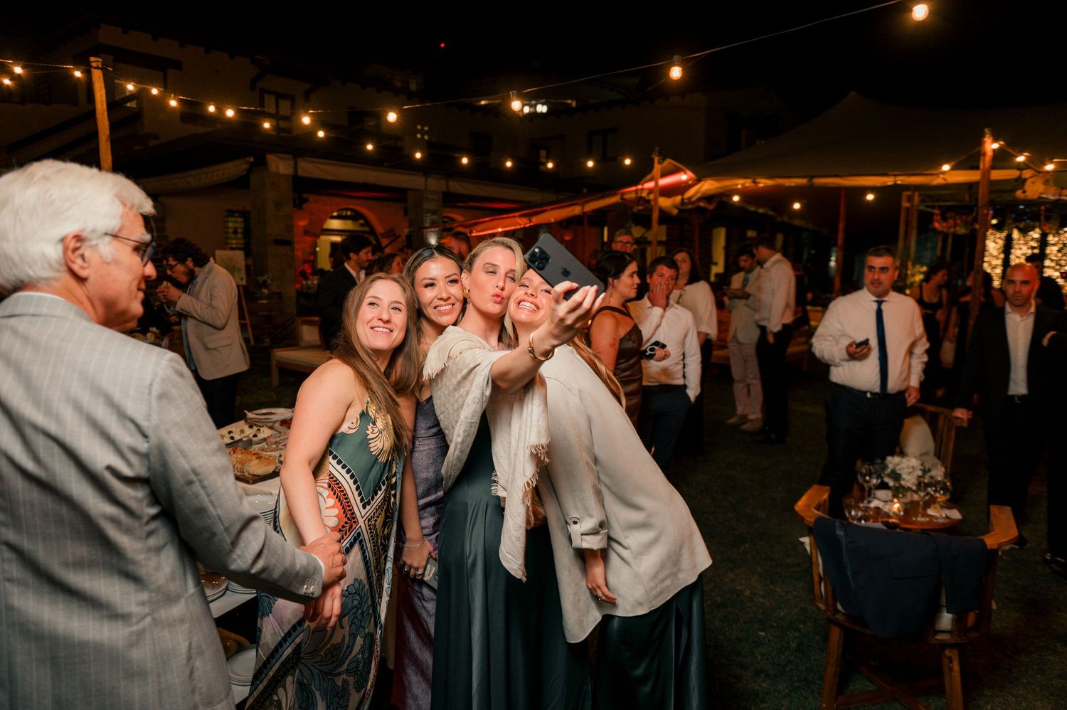 Wedding guests dance and celebrate on an outdoor dance floor under string lights during an evening reception.