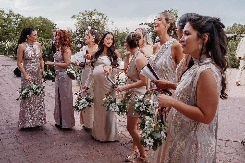 Wedding party members in blush and neutral dresses gather outdoors for candid photos with floral bouquets. wedding in mendoza