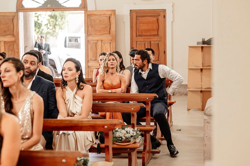 Wedding guests seated on wooden pews in a rustic venue react emotionally during a ceremony. wedding in mendoza