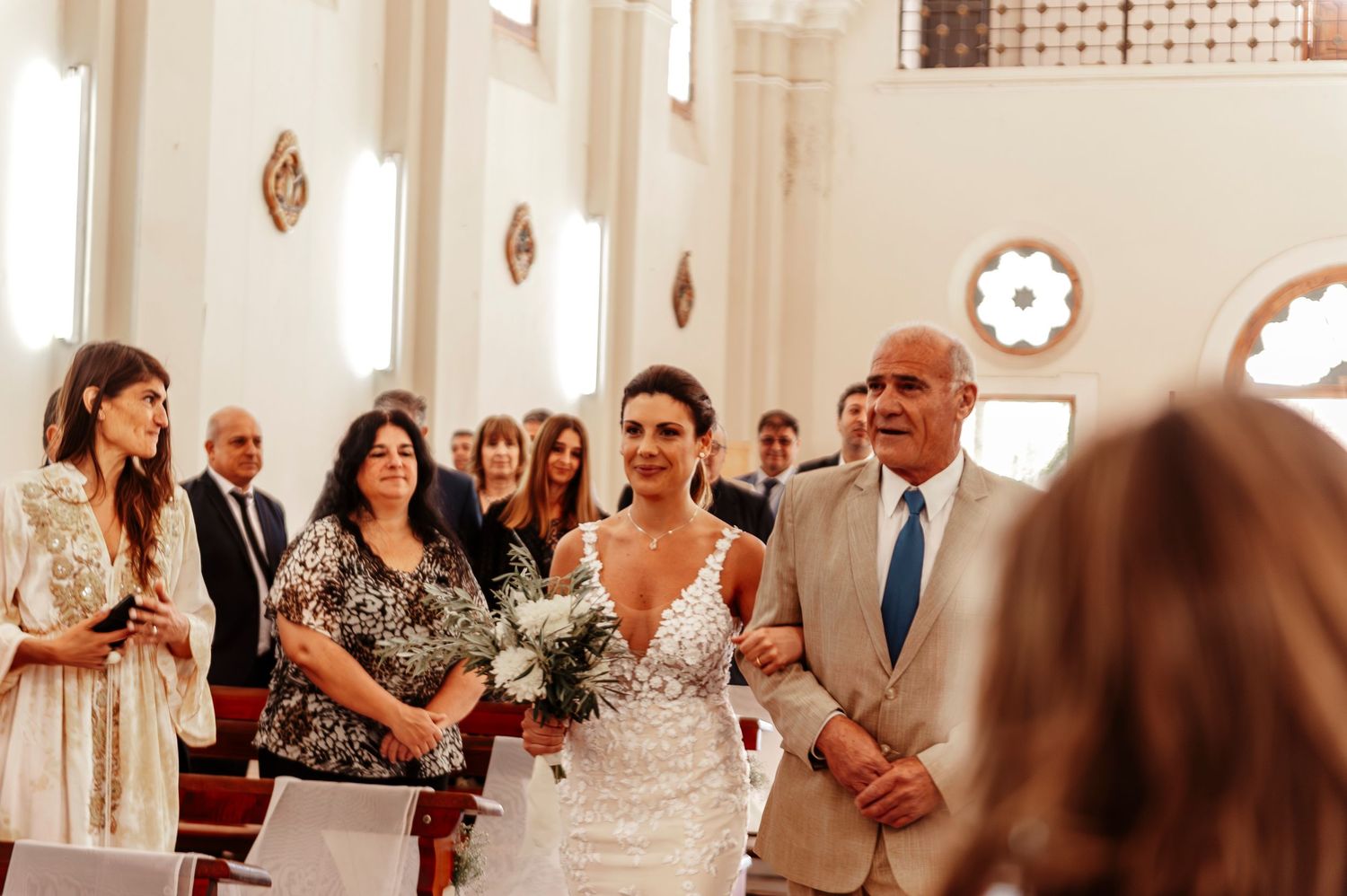 A wedding ceremony takes place inside a traditional church with ornate stained glass windows and decorative wall details.