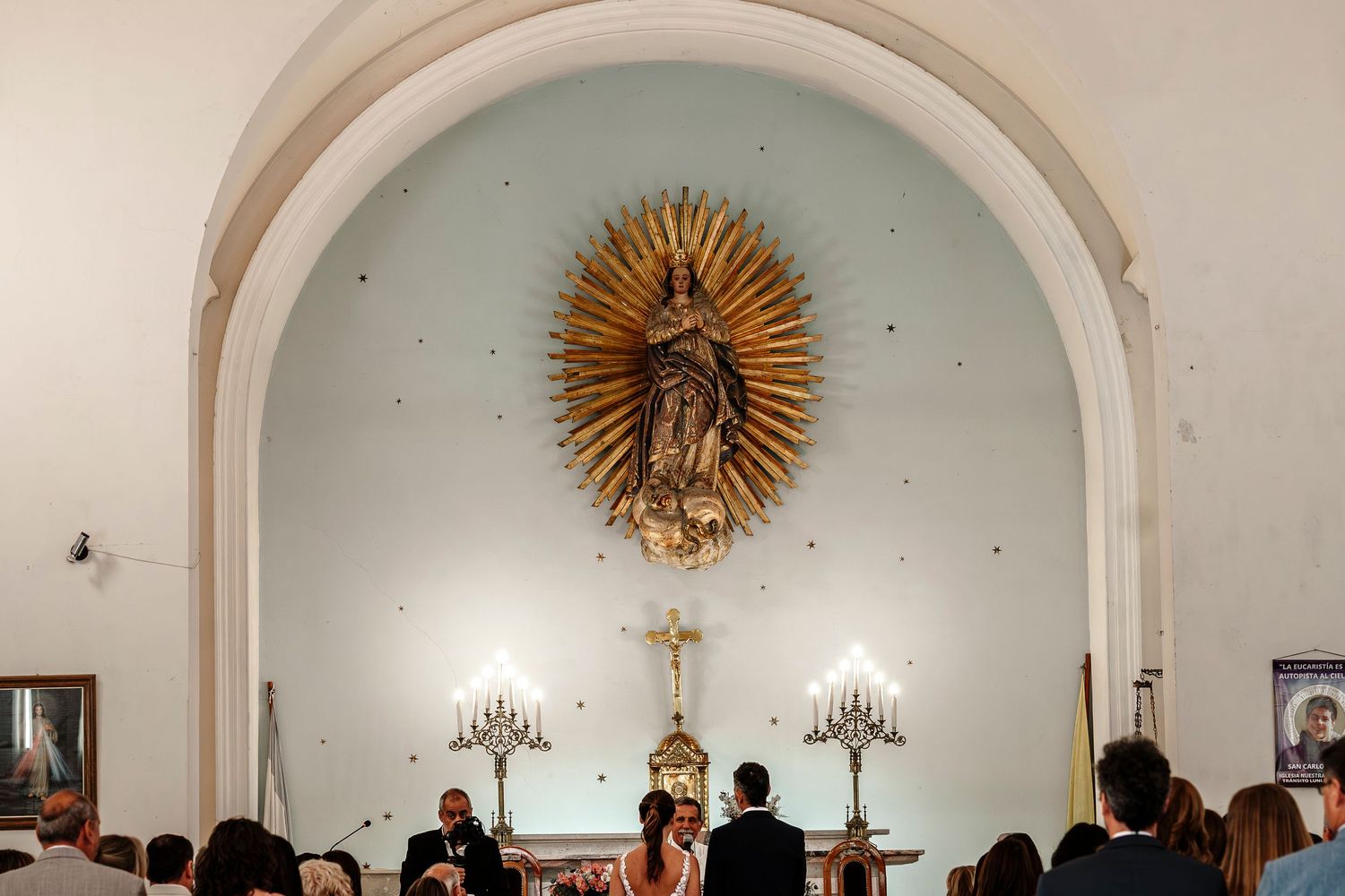 Interior of a traditional church sanctuary with white arched ceilings and ornate gold sunburst decorations.