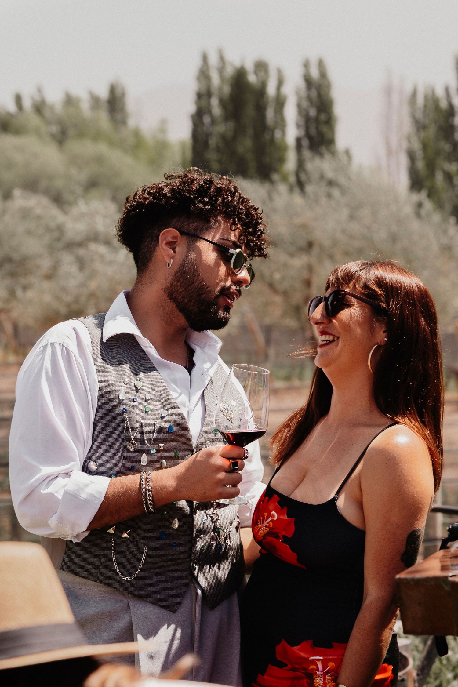 A romantic couple in formal attire shares intimate moments while enjoying wine outdoors in the desert.