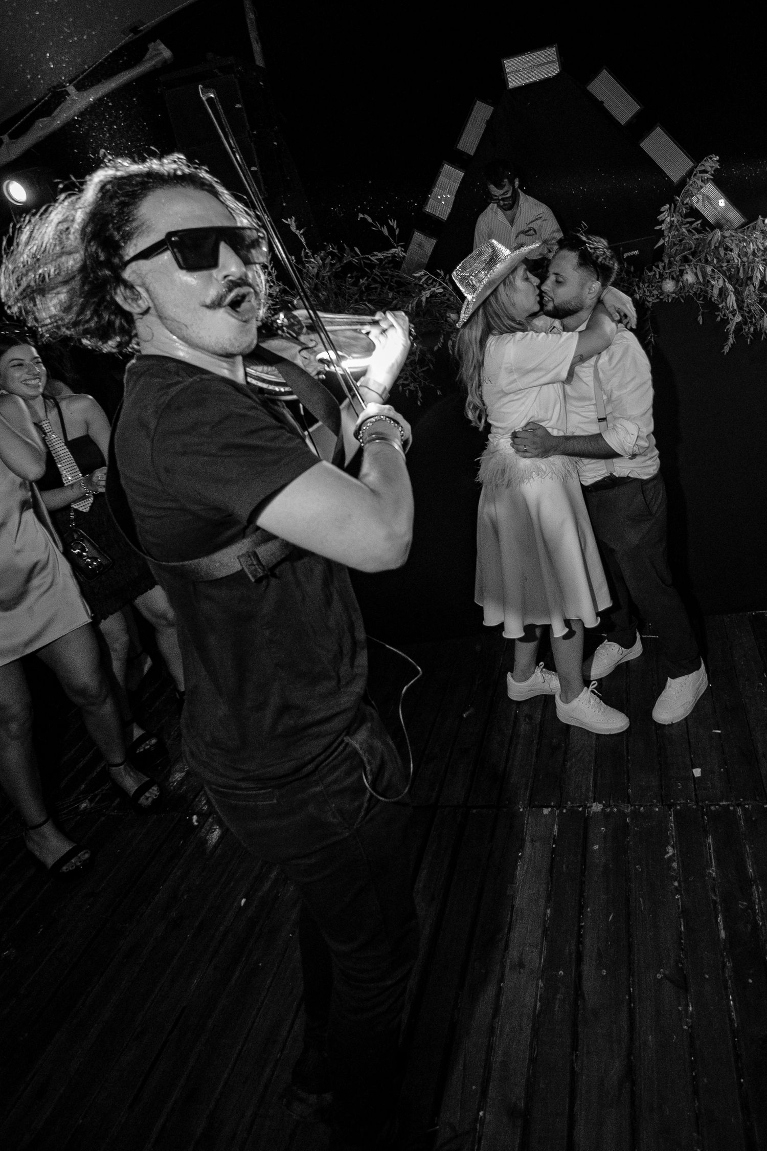 A group of people dance together in a dimly lit venue during what appears to be a lively social gathering.