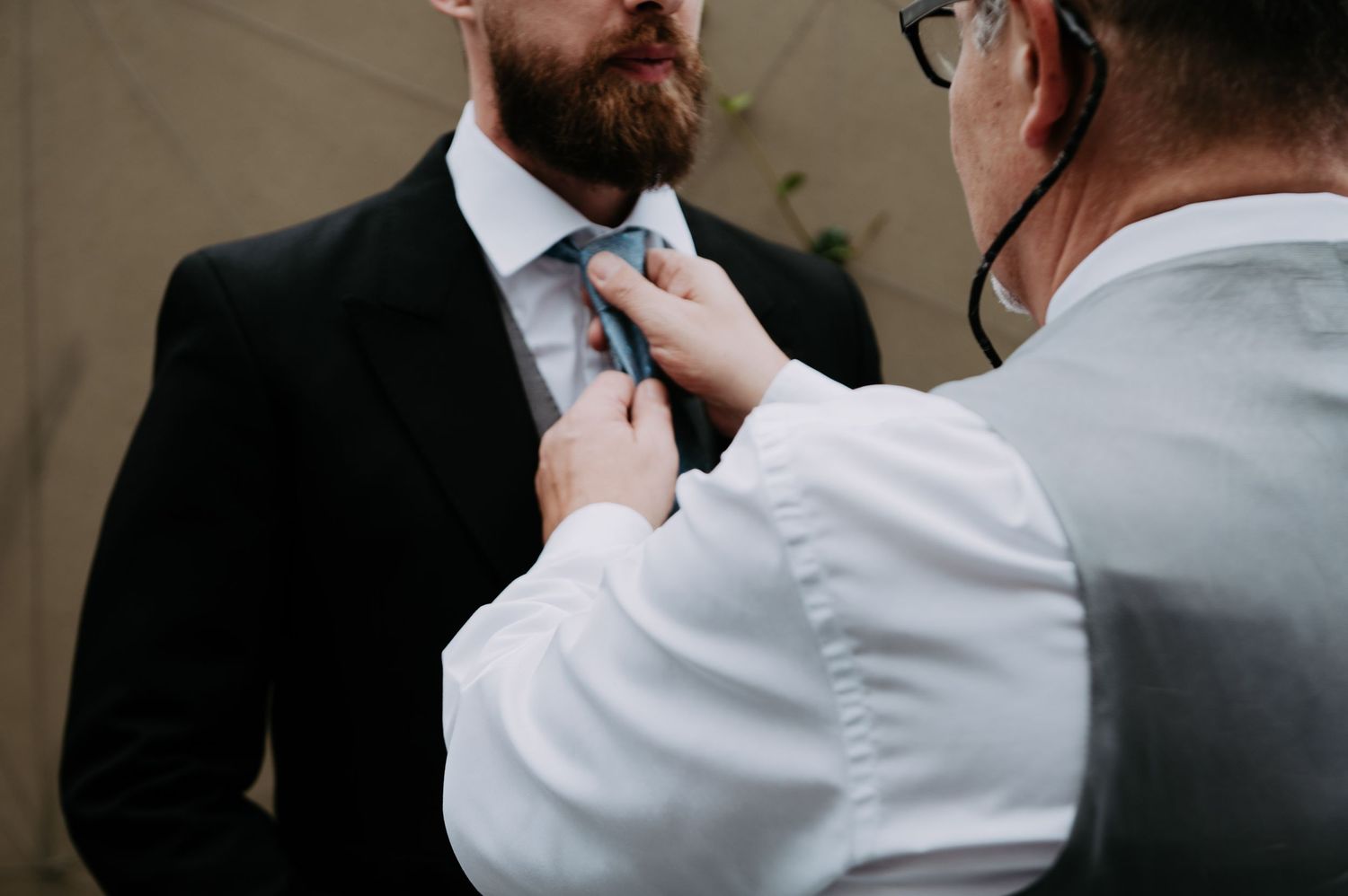 Someone in a white shirt adjusts a light blue necktie on a person wearing a dark suit.