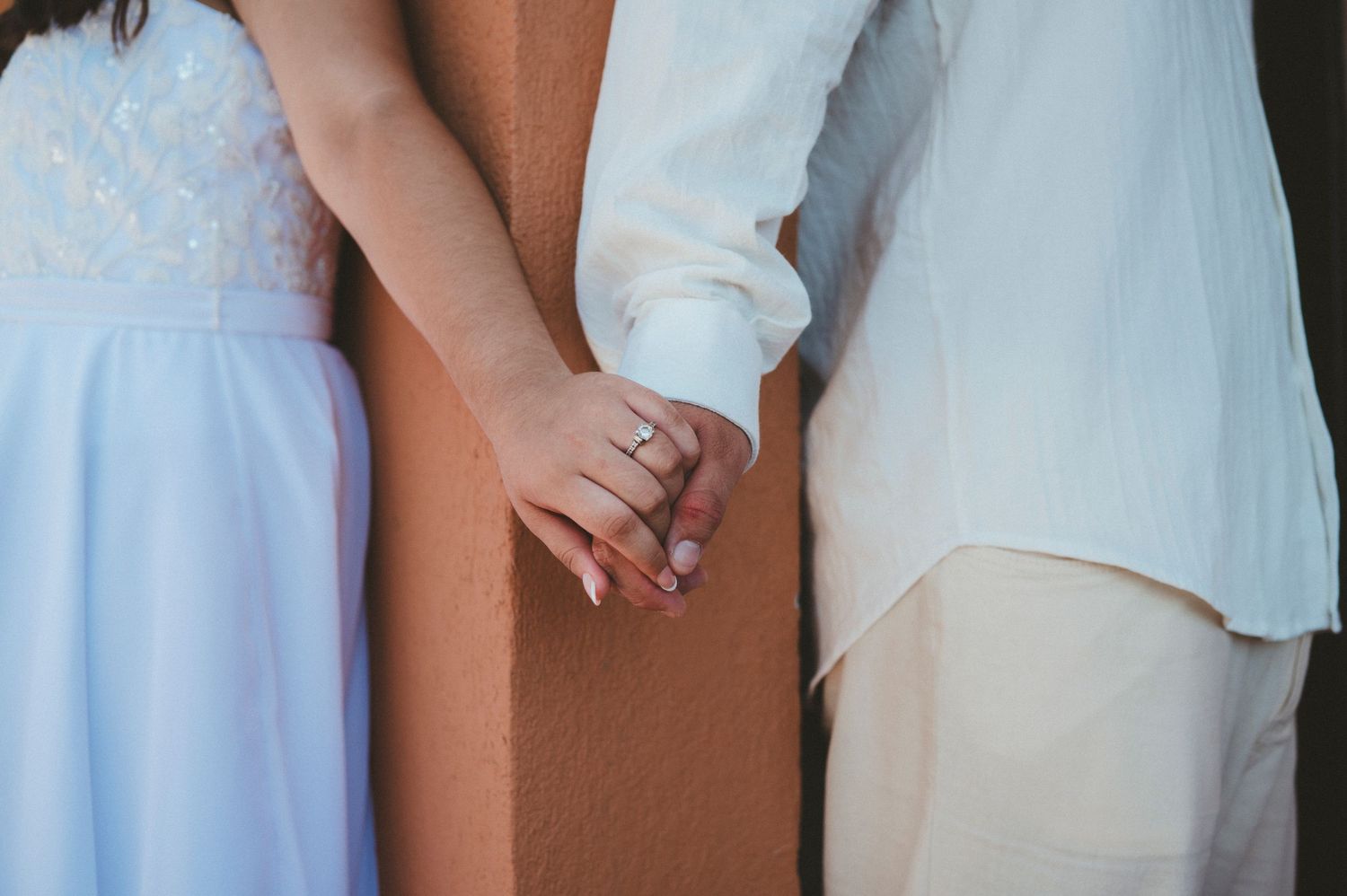 Close-up of a couple holding hands romantically, showing pale blue dress and white clothing.