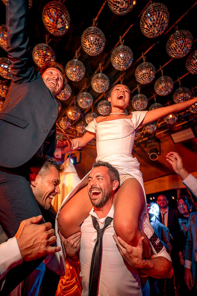People dancing and celebrating at a nightclub with hanging decorative lights creating an energetic party atmosphere.
