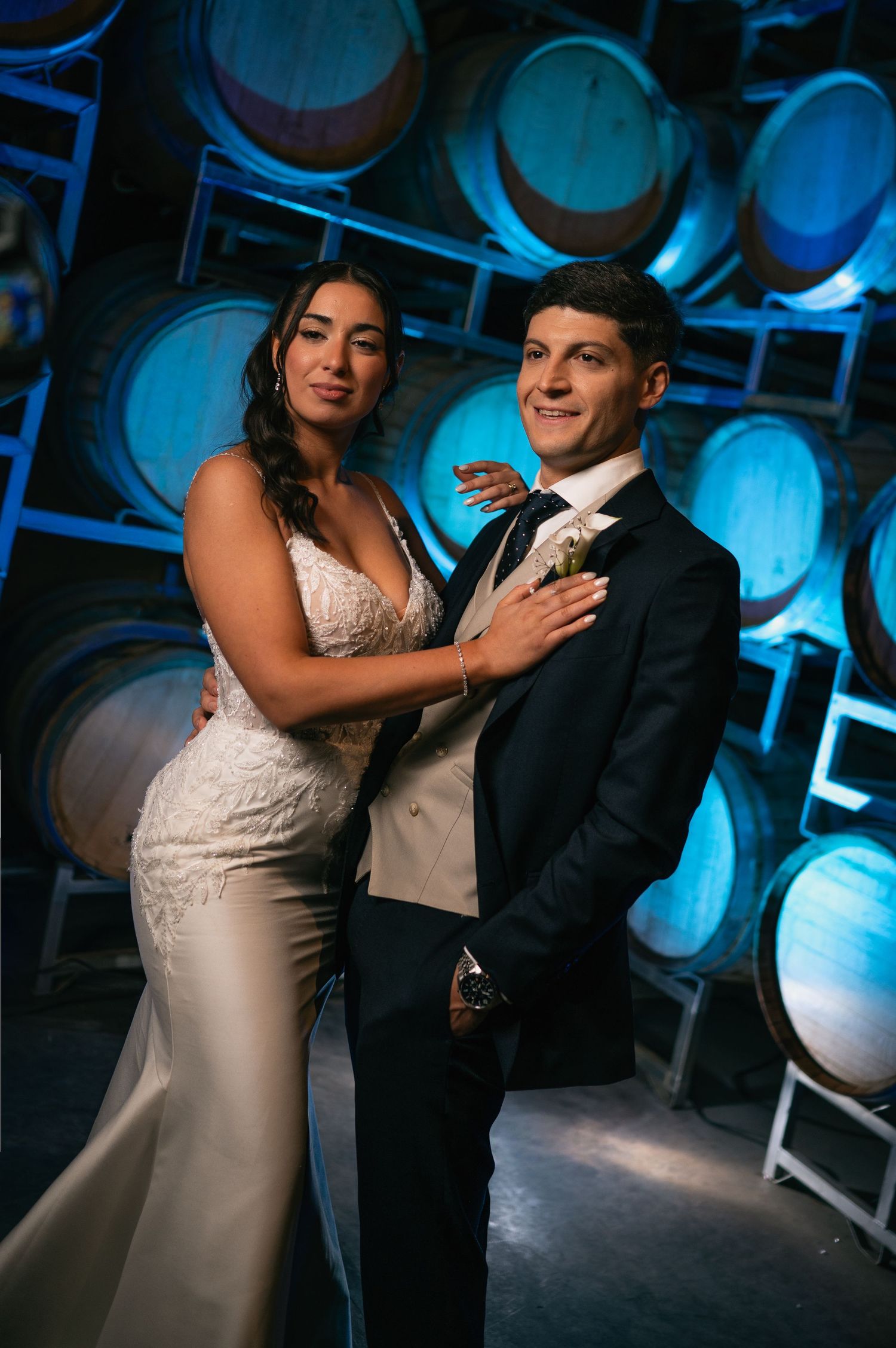 Bride and groom posing elegantly in front of wine barrels with blue lighting at a winery wedding venue.