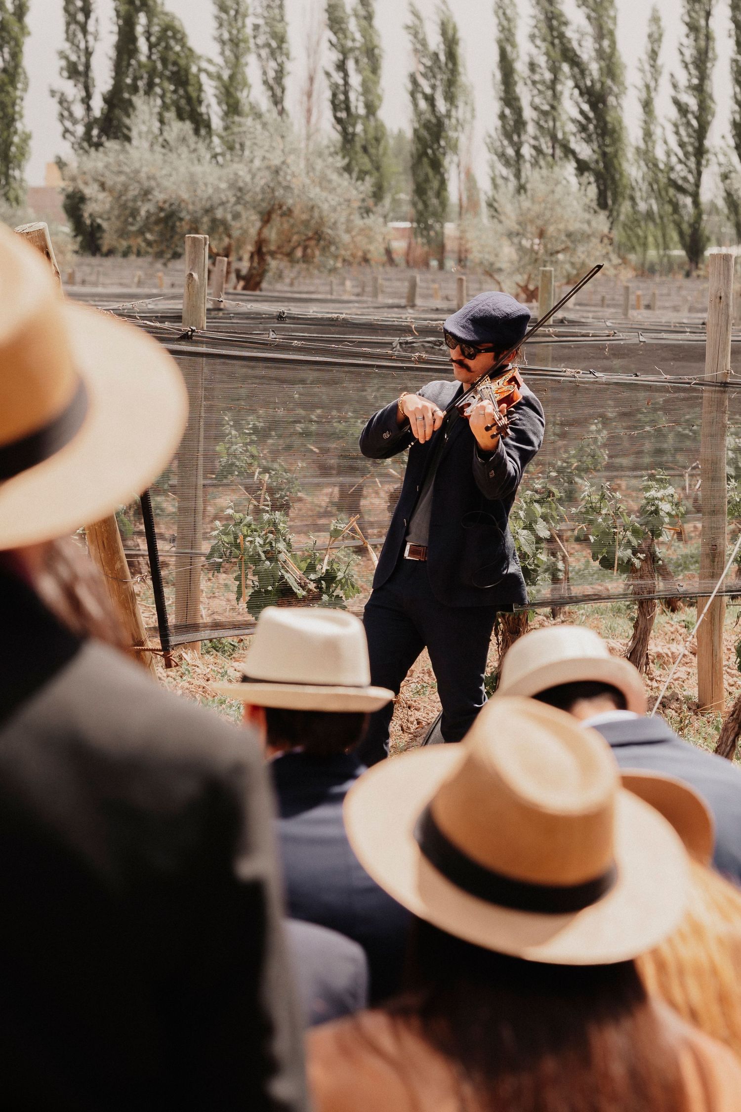 A group wearing cowboy hats listens attentively to someone speaking at an outdoor gathering.