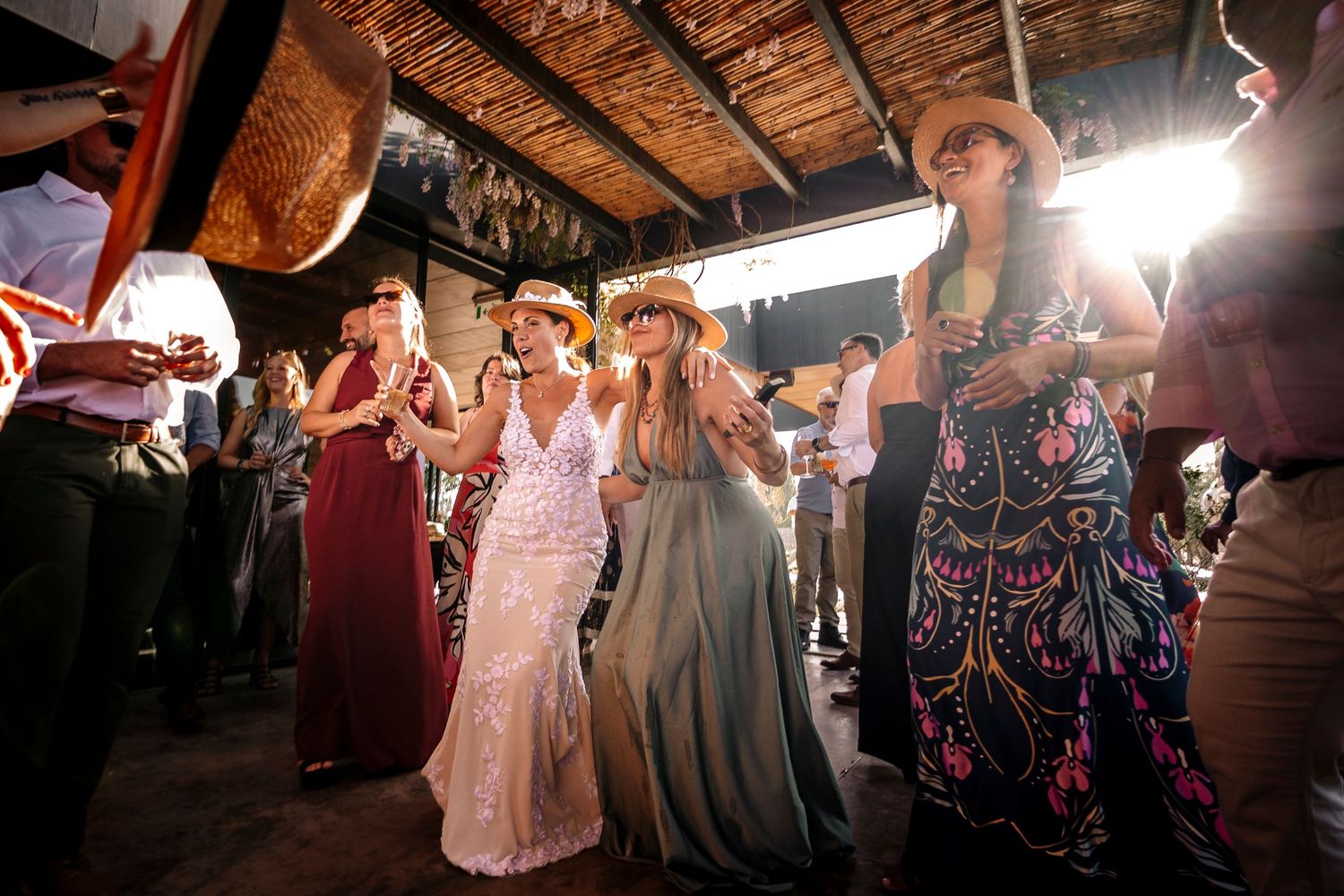 Party guests dancing and celebrating at a rustic venue with exposed wooden beams overhead during a festive event.
