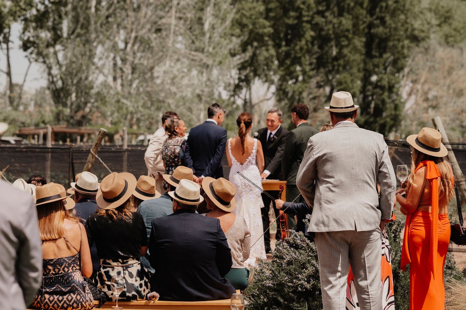 Wedding party in beige and orange attire gathered outdoors for a celebration in a natural setting.