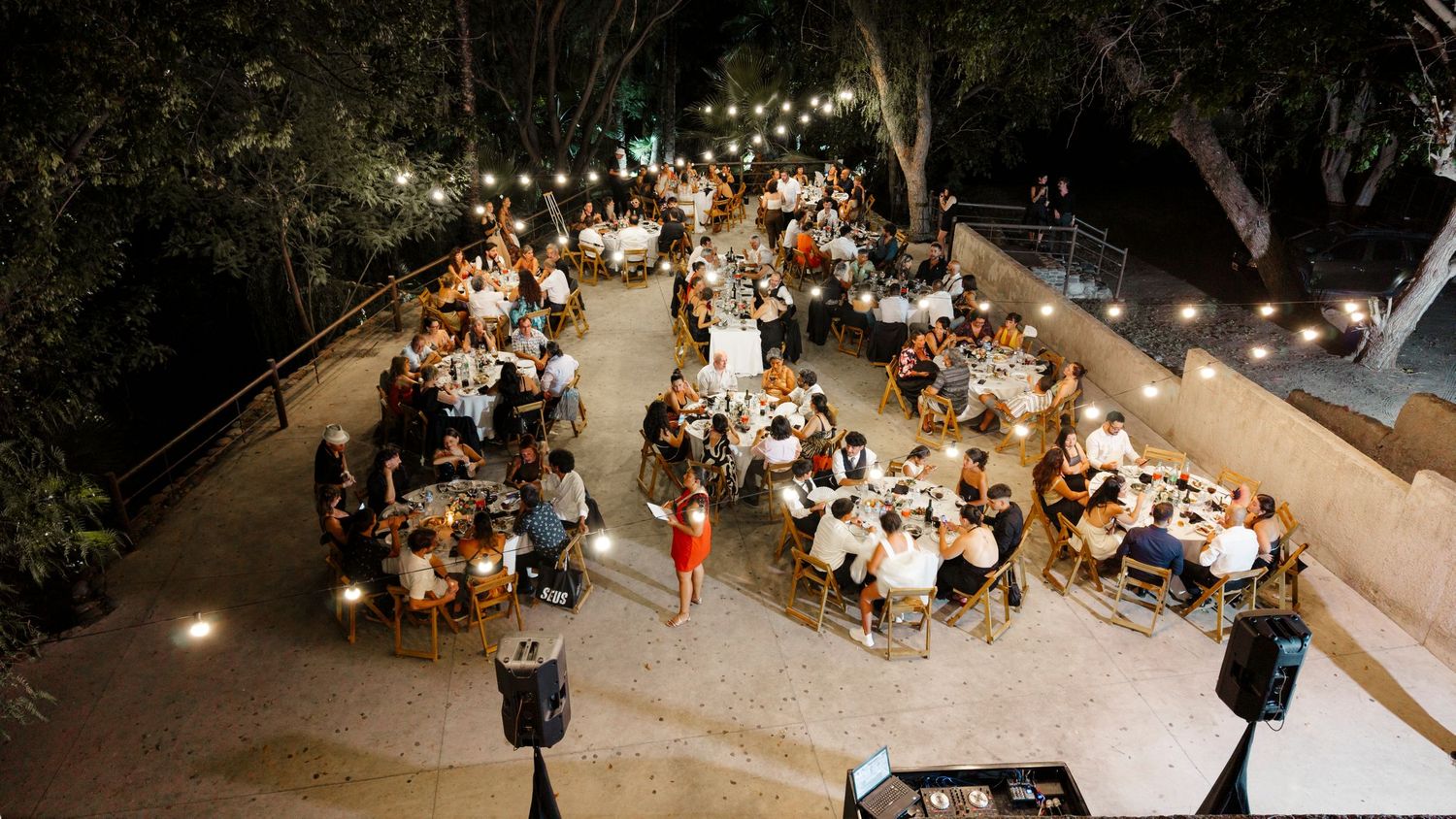 Overhead view of an outdoor evening reception with string lights and guests seated at round tables on a patio.