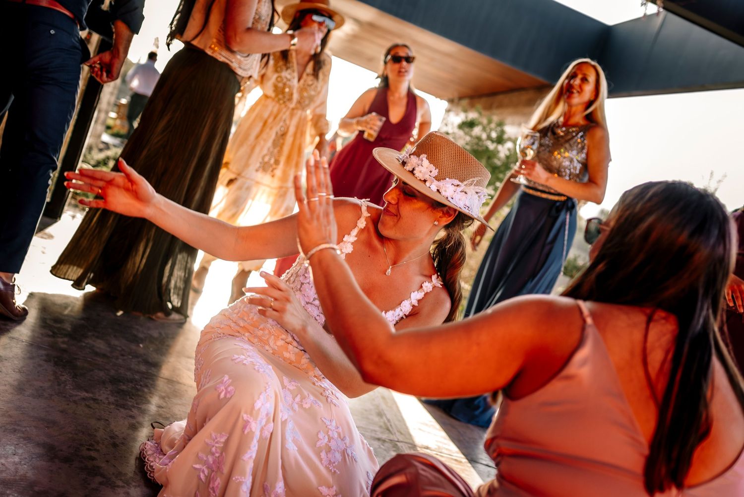 A bride in a pink wedding dress dances with guests during a joyful celebration at an indoor reception venue.