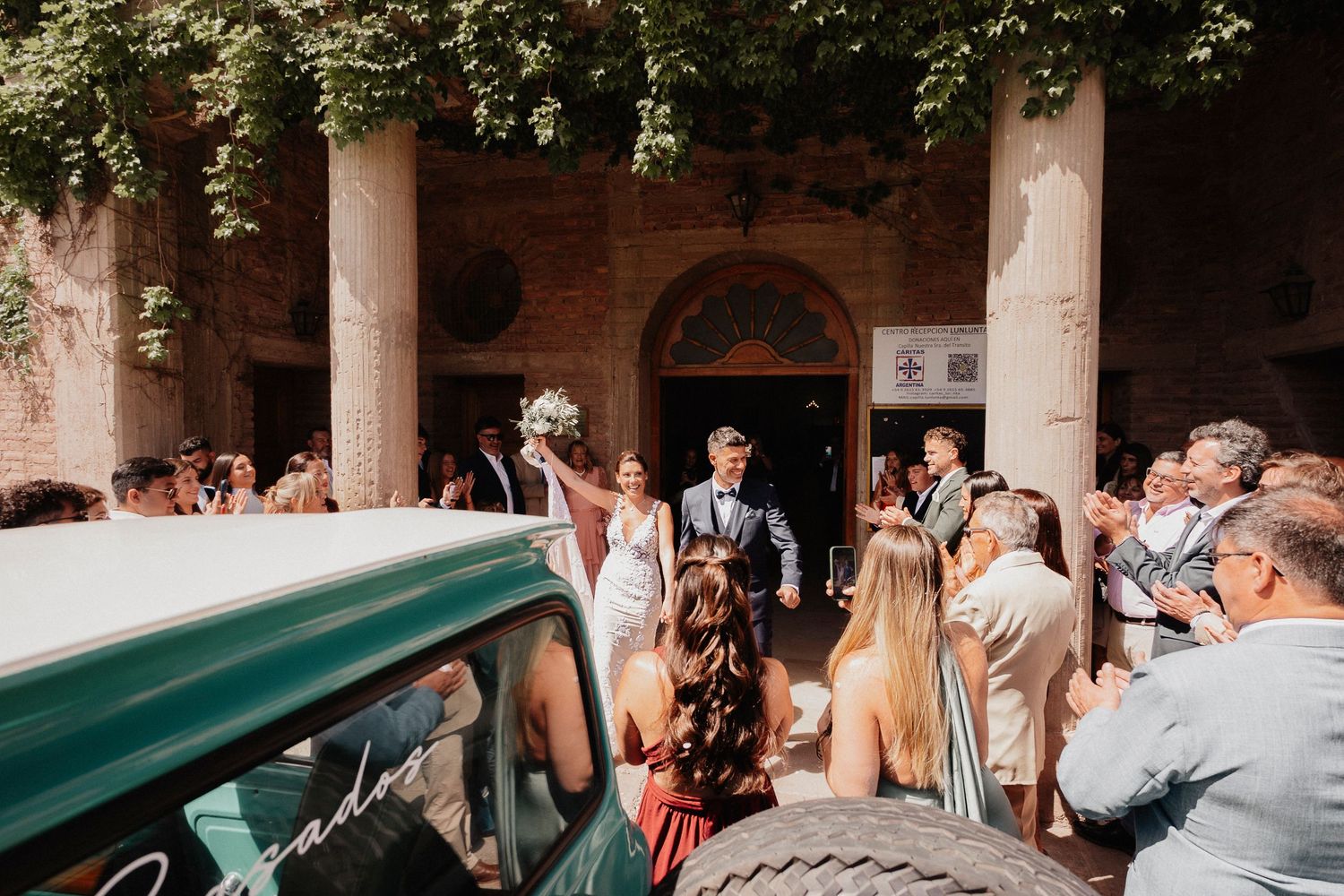 Wedding guests gather under stone columns in an outdoor courtyard during a celebration event.