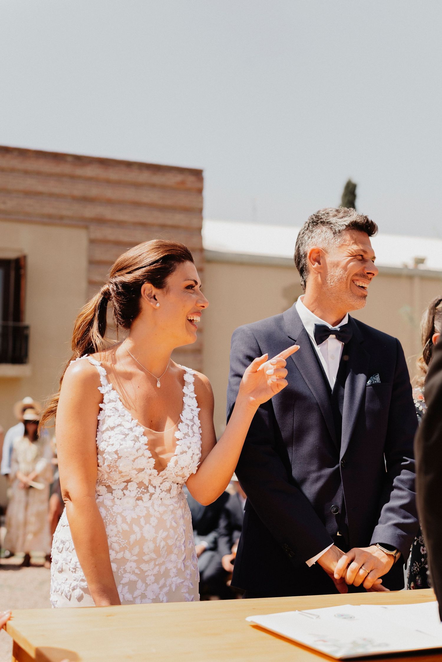 A couple shares a joyful moment during their wedding ceremony at a bright outdoor venue.