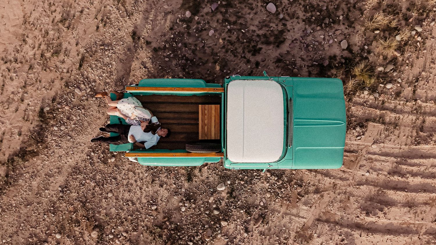 Vintage green car drives along a scenic mountain road with dramatic rocky cliffs and winding turns.