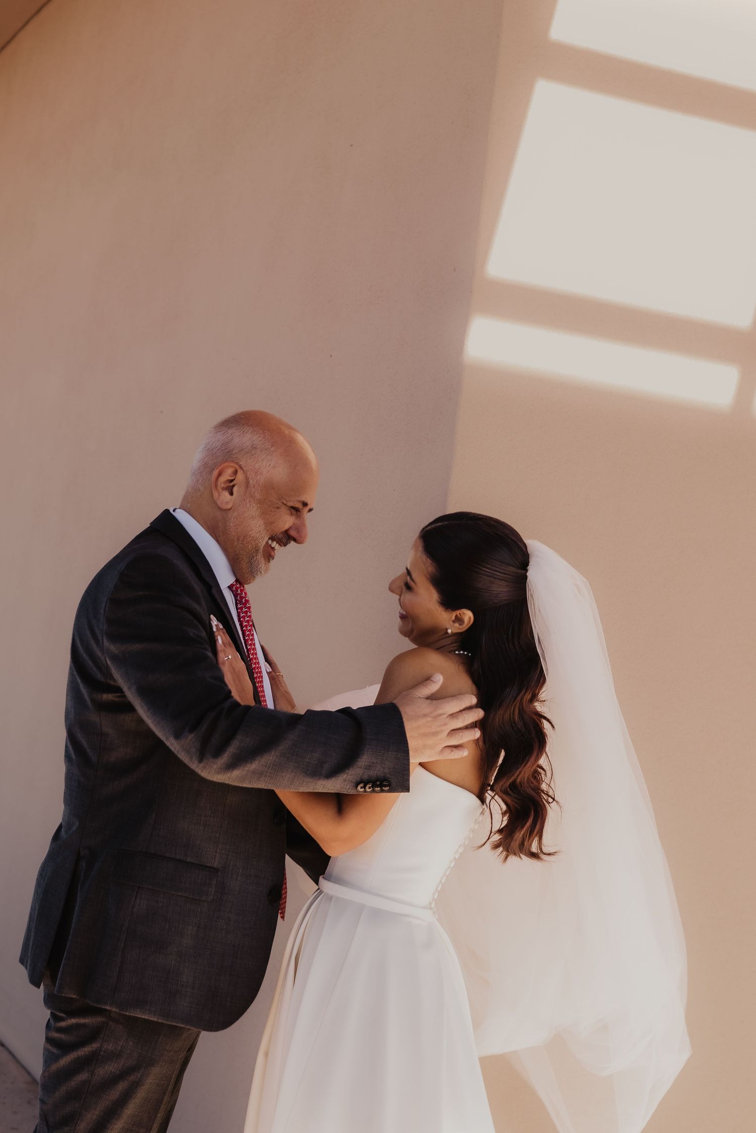 Bride in white gown and veil shares a tender moment with older man in suit during wedding day first look.